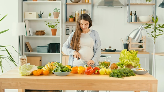 Belle femme enceinte préparant heureusement une salade de légumes Le concept de régime