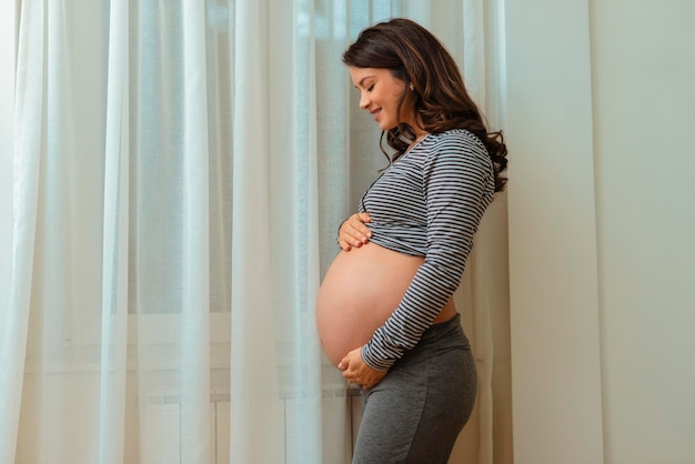 Belle femme enceinte près de la fenêtre à la maison