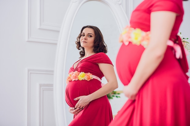 Belle femme enceinte regardant dans le miroir dans la salle lumineuse