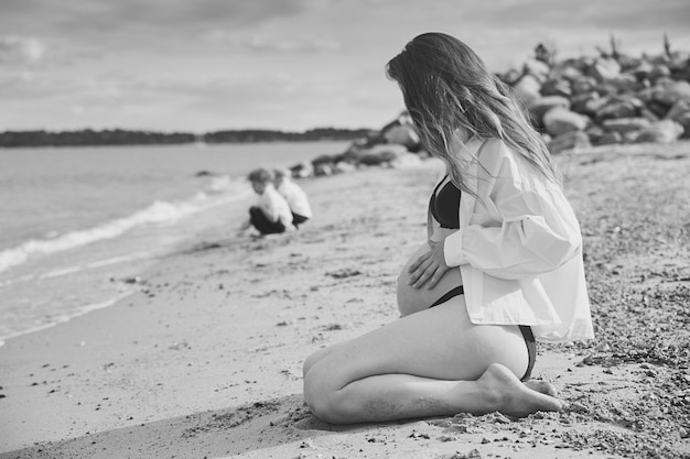 Belle femme enceinte relaxante avec ses fils près de la mer