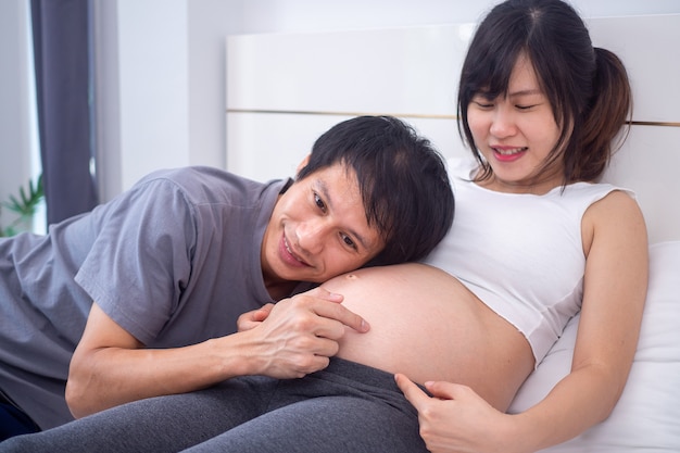 Belle femme enceinte et son mari apprécient et se détendent en jouant avec l'enfant à naître.