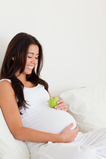 Belle femme enceinte tenant une pomme sur son ventre en position couchée sur un lit