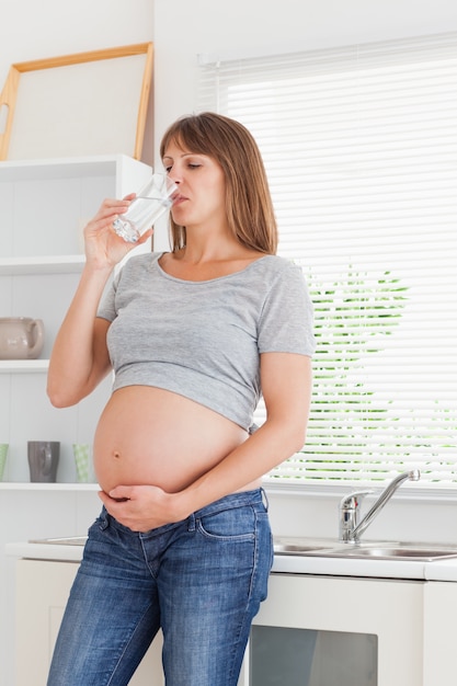 Belle femme enceinte tenant un verre d&#39;eau en se tenant debout