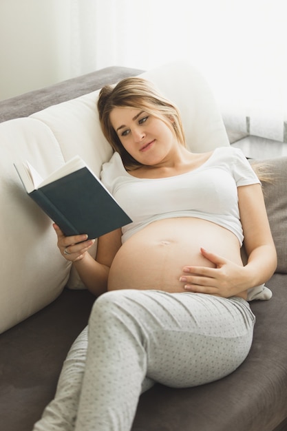 Belle femme enceinte tonique allongée sur un canapé et un livre de lecture