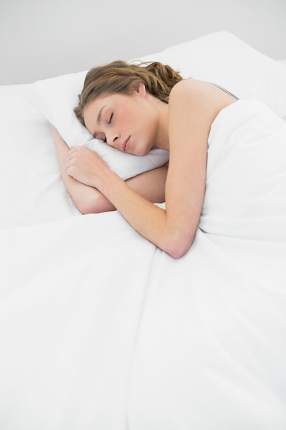 Belle femme endormie se trouvant sous la couverture sur son lit blanc