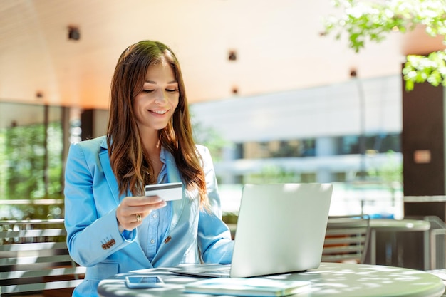 Une belle femme entrepreneure tenant une carte de crédit pour faire des achats en ligne assise sur son lieu de travail dans la rue