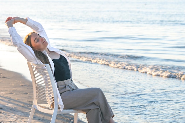 Une belle femme est assise sur une chaise près de la mer