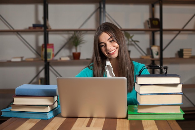 Belle femme est heureuse de son travail réussi avec un ordinateur portable et des livres à la table en bois