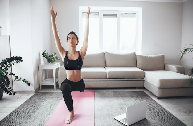 Belle femme étirant ses muscles avant le cours de yoga à la maison pendant la quarantaine avec un ordinateur portable