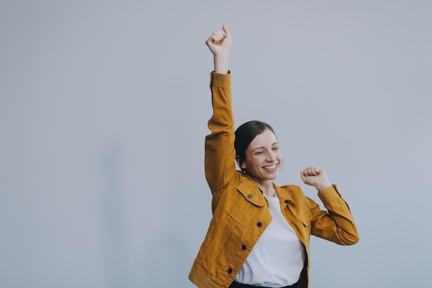 La belle femme européenne aux cheveux bruns émotionnels avec une peau saine et propre sourire charmant vêtue de vêtements légers décontractés écoute et apprécie la musique sur des écouteurs avec une tablette sur un fond blanc