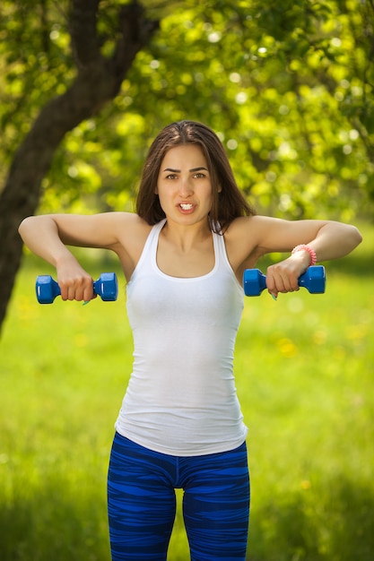 Belle femme exerçant à l'extérieur. Joyeuse fille mince faisant de l'exercice dans le parc en été