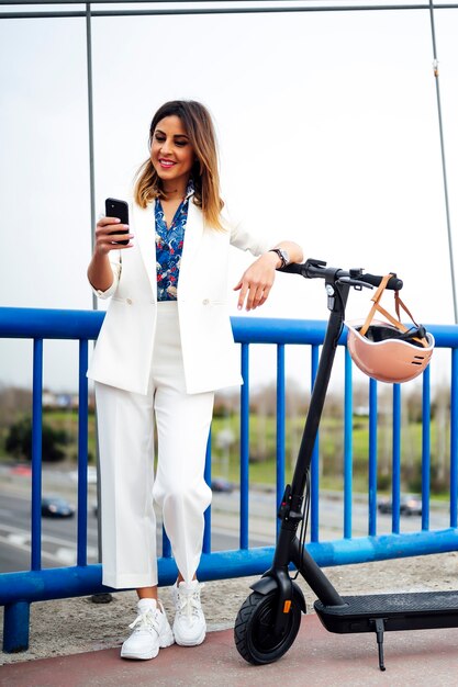 Belle femme à l'extérieur. Jeune femme sur son scooter électrique à l'aide de téléphone