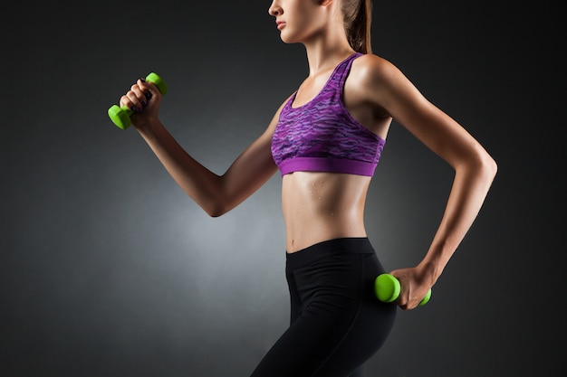Belle femme faisant des exercices de biceps avec des haltères verts. Fond de vignette noir de portrait de studio.
