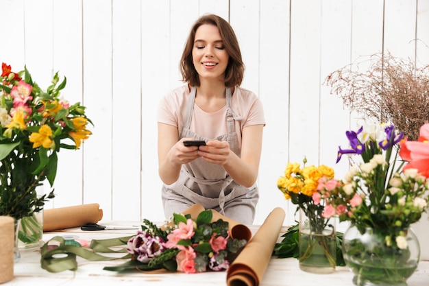 Belle femme fleuriste en tablier travaillant en fleur, et prendre des photos avec un téléphone mobile de bouquet sur la table