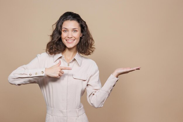 Belle femme sur fond beige sourit et rit fait un geste avec ses mains vers la vente et la promotion latérales