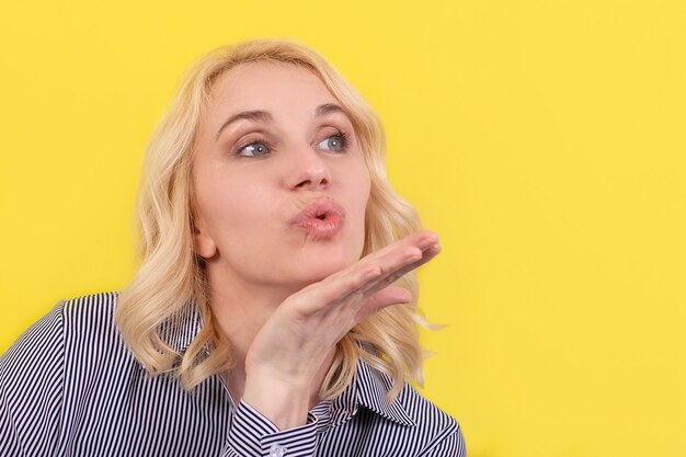 Une belle femme sur fond jaune envoie un baiser aérien Émotions positives Amour