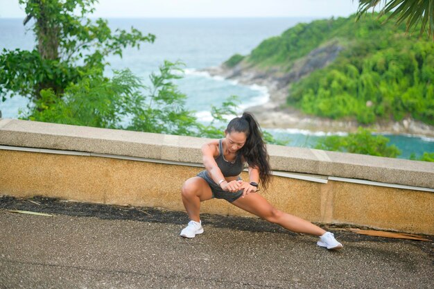 Une belle femme en forme de vêtements de sport faisant de l'exercice sur le sommet de la montagne en bord de mer Concept de santé et de voyage