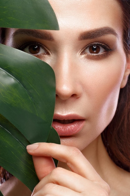 Belle femme fraîche avec une peau parfaite maquillage naturel et feuilles vertes Visage de beauté