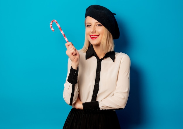 Belle femme française en béret avec sucette bonbon sur le mur bleu