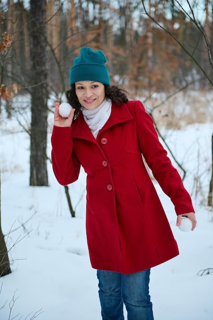 Belle femme gaie dans des vêtements d'hiver chauds et colorés joue des boules de neige dans une forêt enneigée