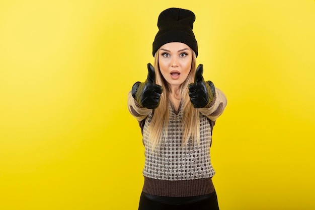 Belle femme en gants noirs et chapeau montrant les pouces vers le haut.