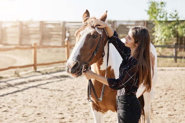 Belle femme gérante de ferme prenant soin et caressant un cheval