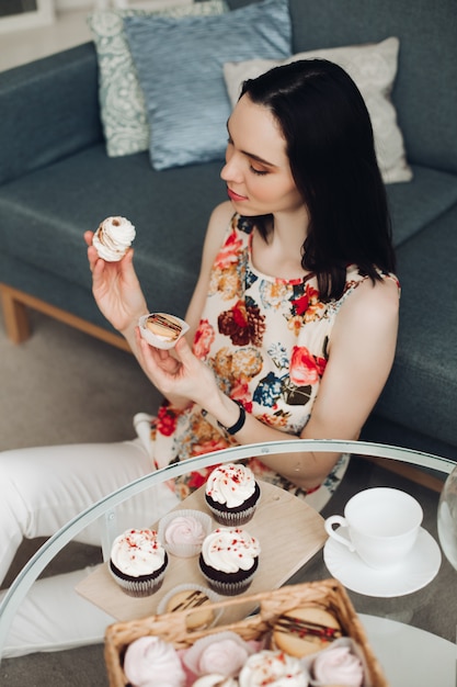 Belle femme avec guimauve dans les mains. Elle est assise à table basse avec des petits gâteaux faits maison.