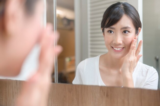 Une belle femme heureuse appliquant une crème hydratante sur le visage, les soins de la peau et le concept de traitement