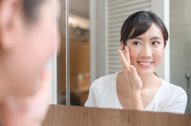 Une belle femme heureuse appliquant une crème hydratante sur le visage, les soins de la peau et le concept de traitement