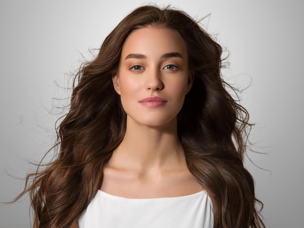 Belle femme heureuse aux cheveux longs en robe blanche sur fond gris de couleur. Portrait de jeune modèle