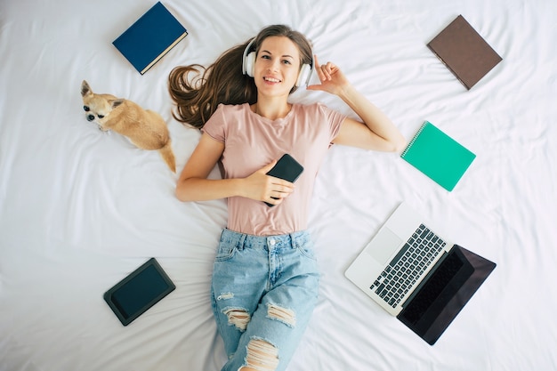 Belle Femme Heureuse Dans Les écouteurs Est Allongée Sur Le Lit Avec Son Mignon Petit Chien Et écouter De La Musique