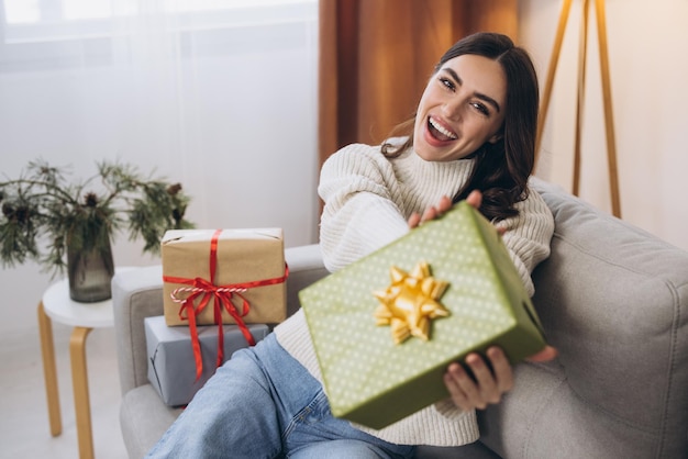 Belle femme heureuse déballant les cadeaux du Nouvel An ou de Noël à la maison sur le canapé
