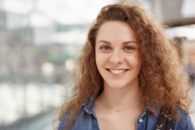 Belle femme heureuse avec une expression gaie, vêtue de vêtements à la mode, pose à l'intérieur, recrée dans le centre commercial