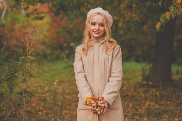 Belle femme heureuse avec des feuilles d'automne dans les mains sur le fond de la nature automnale