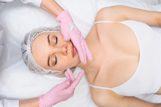 Belle femme heureuse recevant un cosmétologue de traitement de spa dans un salon de beauté avec un gant rose