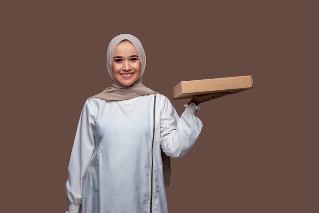 Belle femme en hijab tenant une boîte à pizza avec une main gauche tout en souriant