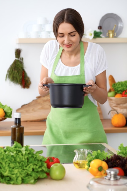 Belle femme hispanique dans un tablier vert cuisinant dans la cuisine. La ménagère a trouvé une nouvelle recette pour sa soupe