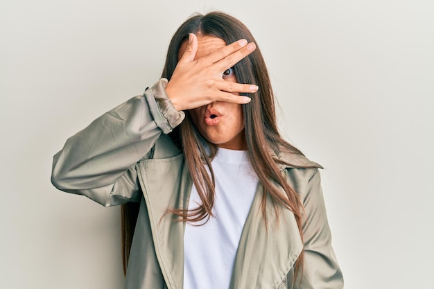 Belle femme hispanique portant des vêtements décontractés furtivement sous le choc couvrant le visage et les yeux avec la main regardant à travers les doigts effrayés