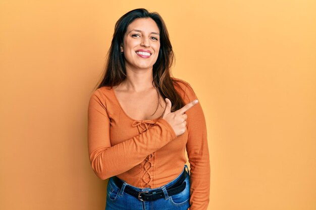 Belle femme hispanique portant des vêtements décontractés souriant joyeux pointant avec la main et le doigt sur le côté