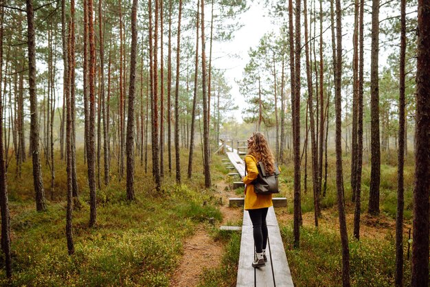 Photo belle femme en imperméable jaune se promène le long d'un chemin en bois dans la forêt concept de tourisme récréatif