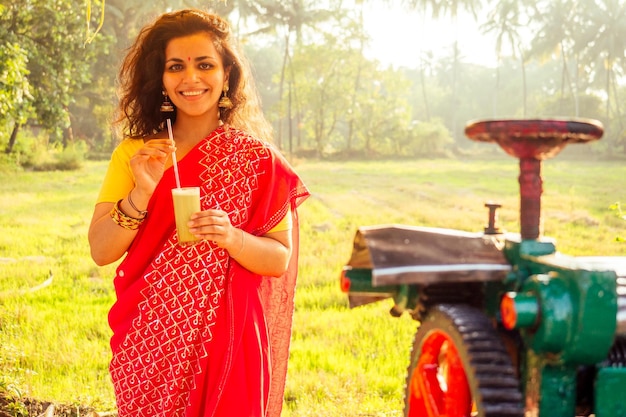 Belle femme indienne en sari rouge debout près de l'appareil de fabrication de jus de canne à sucre plantation été ferme arrière-plan petite entreprise démarrage