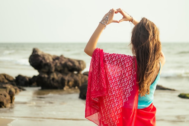 Belle femme indienne en sari rouge remet le symbole du coeur sur la plage. Amour et foi de la Saint-Valentin
