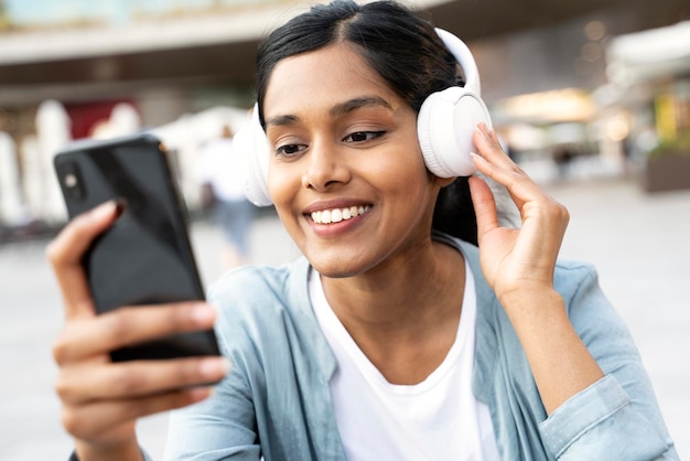 Belle femme indienne souriante tenant un téléphone portable écoutant de la musique dans des écouteurs sans fil