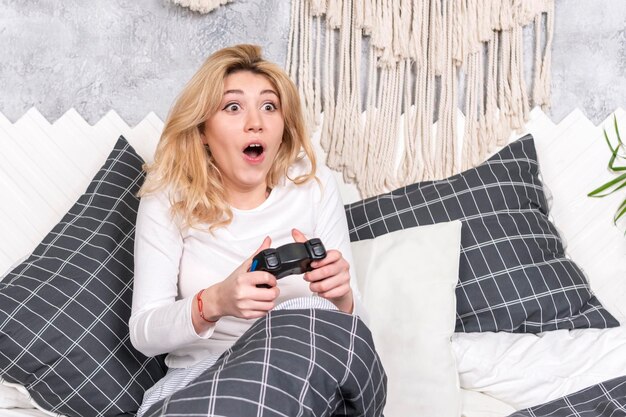 belle femme de jeu joue le jeu avec le joystick assis sur le lit