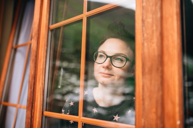 Photo belle femme avec joli visage regarde à travers la fenêtre réfléchie