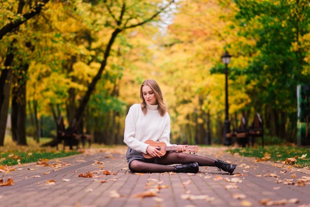 Belle femme jouant de la guitare ukulélé à l'extérieur dans la forêt d'automne