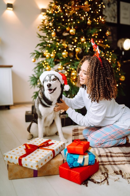 Belle femme jouant, s'amusant avec son chien assis près de l'arbre de Noël Vacances d'hiver.