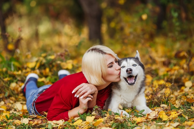 Belle femme joue avec un chien husky dans la forêt d'automne