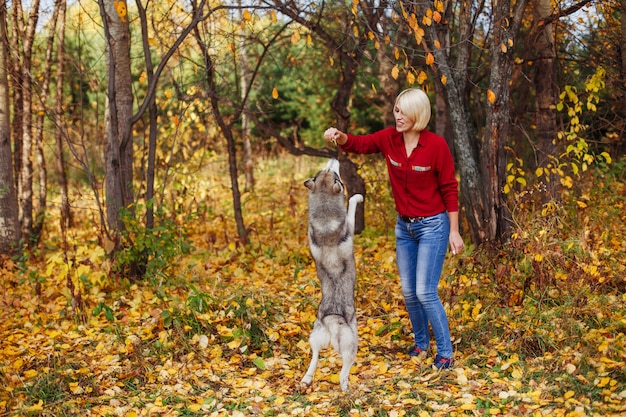 Belle femme joue avec un chien husky dans la forêt d'automne