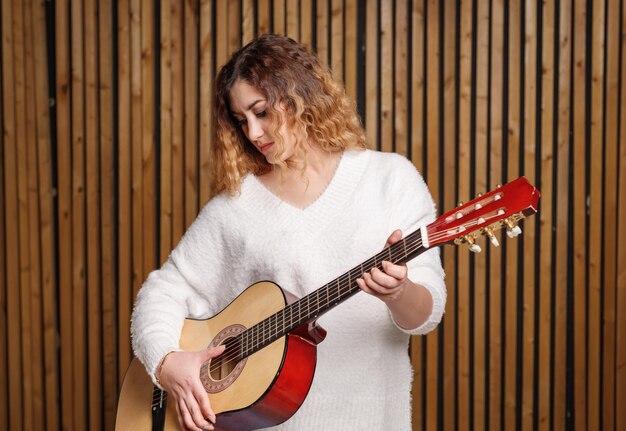 Une belle femme joue de la guitare classique, sur fond de mur en bois